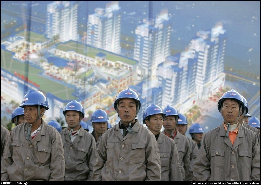 Labourers stand in front of a poster featuring a commercial plaza during a ceremony marking the start of its construction in Kunming